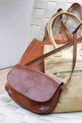 Two leather bags, one brown and one beige, on a woven chair.